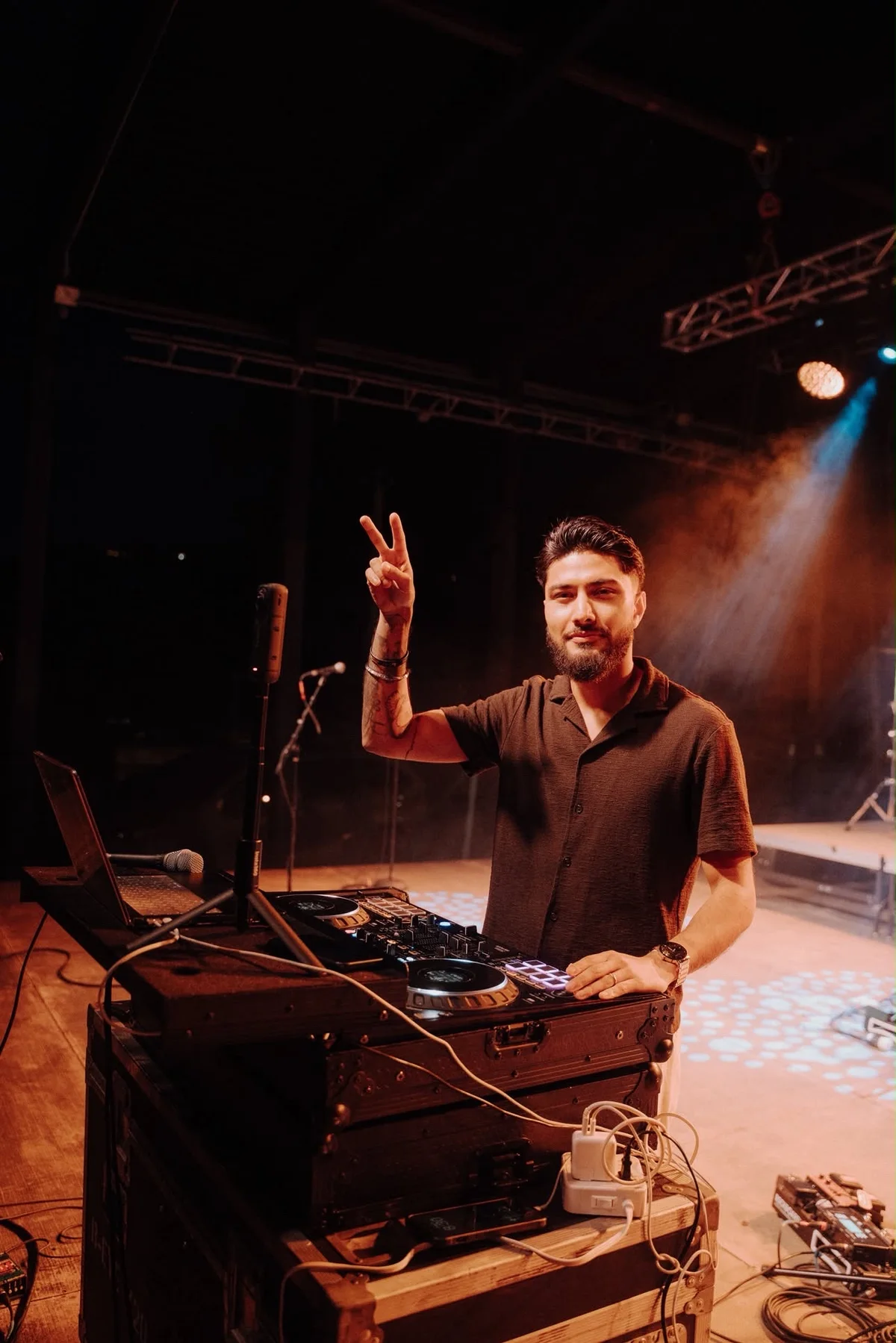 DJ Sarif raising a peace sign behind the decks on stage